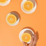 Oranges on in plates on a bright table and a woman's hand. Minimal food concept. Flat lay.